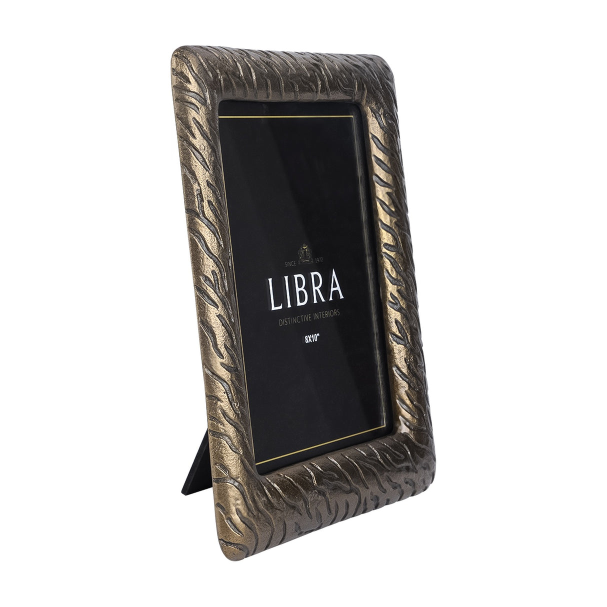 Libra Interiors etched cast aluminium 8x10 photo frame in antique brass, shown upright in portrait orientation with fold-out easel back on a white background.