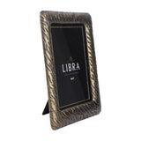 Libra Interiors etched cast aluminium 8x10 photo frame in antique brass, shown upright in portrait orientation with fold-out easel back on a white background.