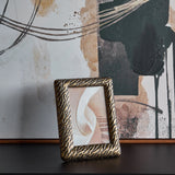 Libra Interiors Etched Tiger cast aluminium 5x7 photo frame in antique brass, displayed upright on a dark surface against abstract artwork.