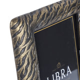 Close-up of the Libra Interiors Etched Tiger cast aluminium frame corner, showing raised tiger-stripe texture in an antique brass finish with warm gold tones.