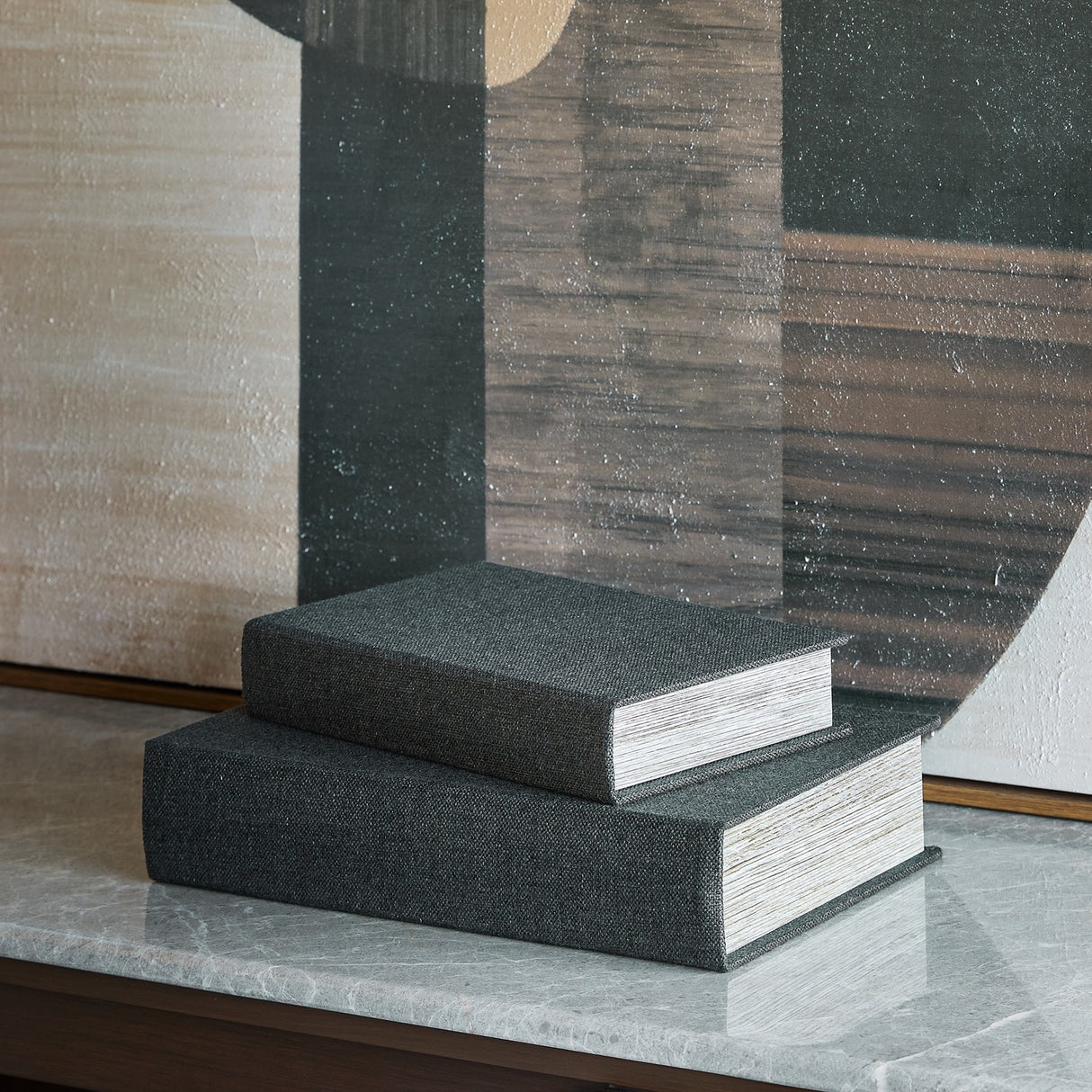 Libra Interiors black book-style linen storage boxes stacked on a marble console with abstract art behind, showing woven covers and page-edge sides.