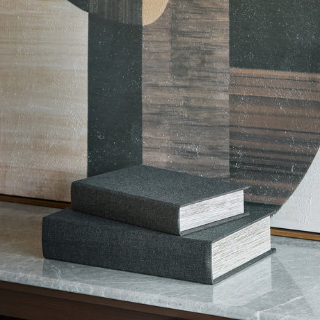 Libra Interiors black book-style linen storage boxes stacked on a marble console with abstract art behind, showing woven covers and page-edge sides.