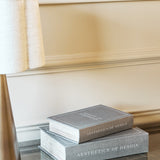 Libra Interiors Linen Book-Style Storage Boxes in grey stacked on a marble surface beside a lamp base, set against a cream panelled wall.