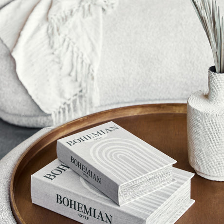 Libra Interiors Linen Book Style storage boxes in taupe with black Bohemian lettering and white arch motif, stacked on a wooden tray beside a textured vase.