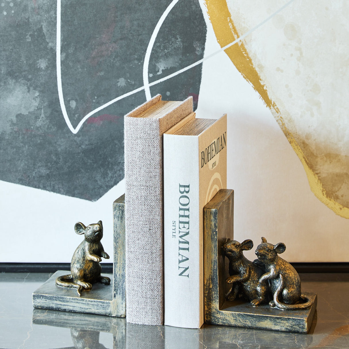 Libra Interiors Rough Cast Mouse Bookends in antique gold resin, one with a standing mouse and one with two seated mice, holding books on a shelf.