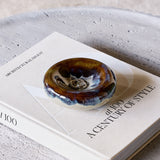 Libra Interiors Reactive Glaze Stoneware Bowl in blue and smoky grey, holding rings, styled on an Architectural Digest book beside a stone tray.