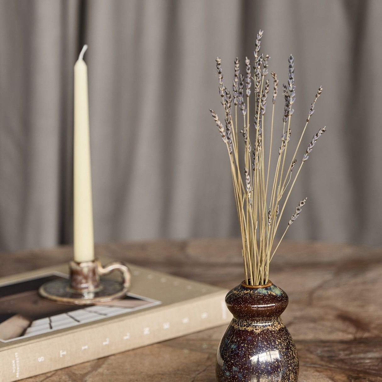 Libra Interiors Reactive Glaze Gourd Stoneware Vase in speckled brown with gold flecks, holding dried lavender stems beside a taper candle and book.