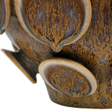 Close-up of Libra Interiors Reactive Glaze Raised Circle stoneware planter in brown, showing mottled glossy glaze pooling across the raised circular discs.