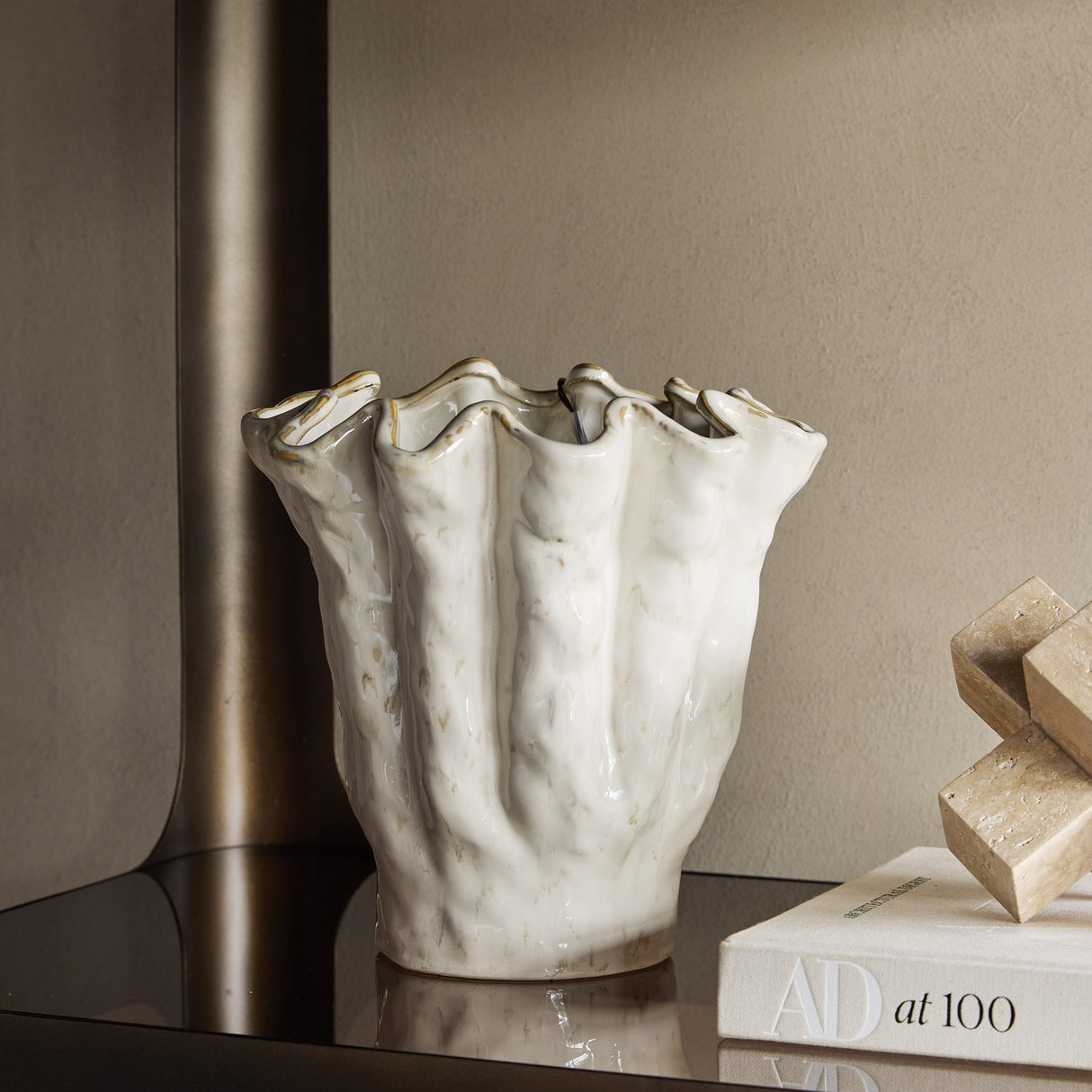 Libra Interiors Ruffled Ceramic Wavy Vase in cream with glossy reactive glaze and golden-brown speckled rim, styled on a dark console with books.