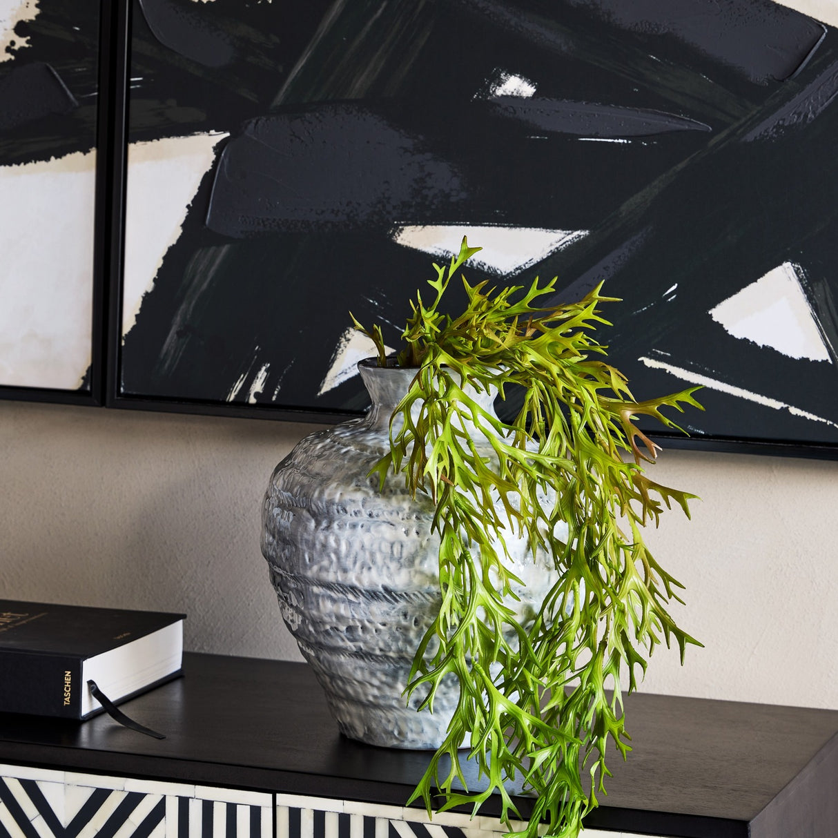 Libra Interiors Textured Glaze Wash ceramic vase in white with a trailing green fern, styled on a dark console beneath bold black brushstroke artwork.