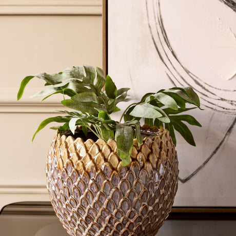 Libra Interiors Scale-Textured Ceramic Planter in brown, holding leafy foliage on a console beside abstract framed art and cream panelling.