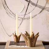 Libra Interiors Petal reactive glaze ceramic candle holders in brown, sculpted as tropical blooms holding cream taper candles atop a book by abstract art.
