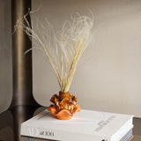 Libra Interiors Reactive Glaze Ceramic Wavy Small Vase in brown and orange with dried grasses, styled on a design book beside a bronze frame.
