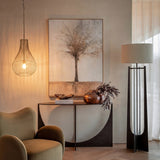 Libra Interiors Burnished Brass Wire Pear Drop Pendant Light illuminated beside a tree artwork, curved console with copper vase, and tall floor lamp.