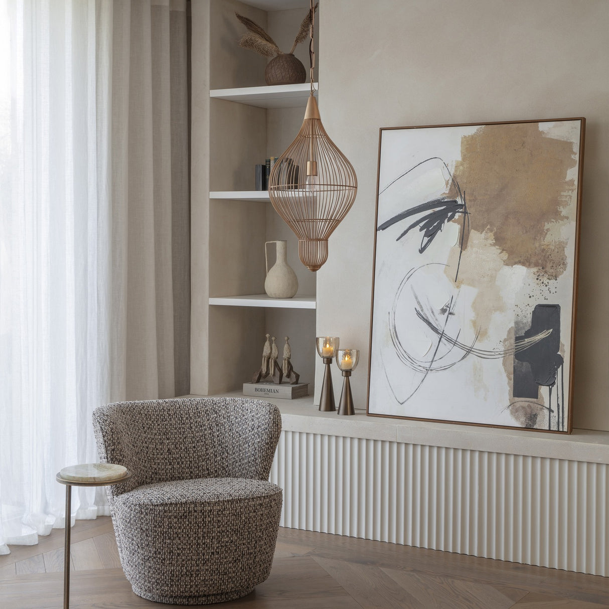Libra Interiors Teardrop Wire burnished brass pendant light hanging beside open shelving in a neutral living room with a bouclé armchair and abstract artwork.