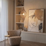 Libra Interiors Teardrop Wire Burnished Brass Pendant Light illuminated above a bouclé armchair, alcove shelving and abstract artwork in a neutral living room.
