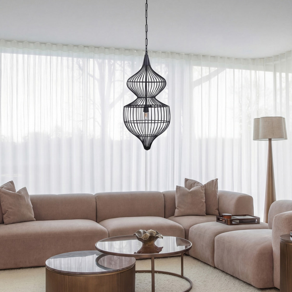 Libra Interiors Wire Cage Double Tiered Pendant Light in black steel hangs above a beige sectional sofa and round coffee tables in a bright living room.
