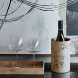 Libra Interiors Burl Veneer Brass-Lined Wine Rack in natural finish holding a wine bottle beside two stemmed glasses on a wooden tray with abstract art behind.