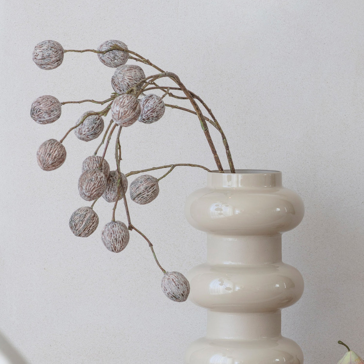 Libra Interiors Tiered Enamel Iron Vase in cream with stacked rounded forms, holding a branch of textured berries against a pale neutral background.