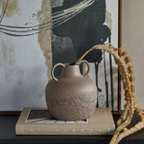 Libra Interiors Textured Two-Tone Iron Handled Vase in brown with looped handles and rough base, styled on a book beside dried stems and abstract art.