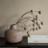 Libra Interiors Textured Two-Tone Handled Metal Vase in brown with dried seed pod branches, styled on a dark sideboard beside an AD at 100 book.