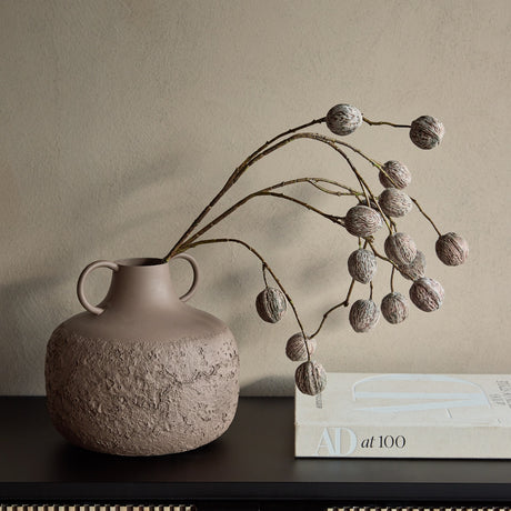 Libra Interiors Textured Two-Tone Handled Metal Vase in brown with dried seed pod branches, styled on a dark sideboard beside an AD at 100 book.