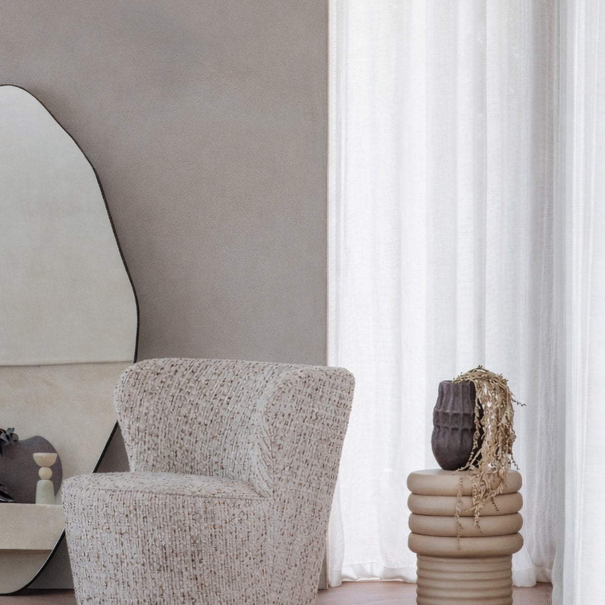 Libra Interiors Ribbed Iron Sculptural Side Table in cream with stacked ribbed base and domed top, styled beside a boucle armchair and sheer curtain.