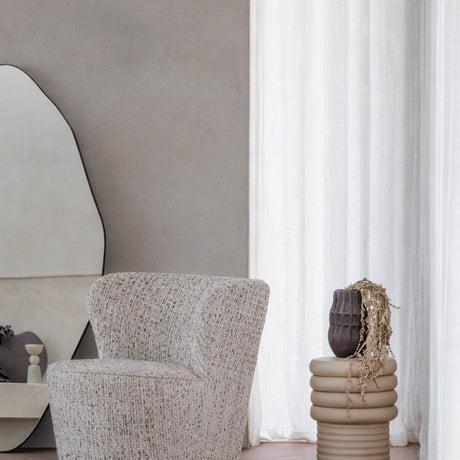 Libra Interiors Ribbed Iron Sculptural Side Table in cream with stacked ribbed base and domed top, styled beside a boucle armchair and sheer curtain.