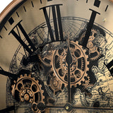 Close-up of Libra Interiors Moving Cogs World Map Wall Clock in antique gold, showing black Roman numerals, exposed brass cogs and sepia map detailing.