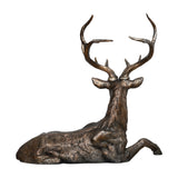 Libra Interiors Textured Resin Lying Stag Sculpture in bronze, shown from behind with head raised and full antlers on show, on a plain background.