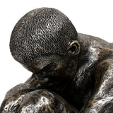 Close-up of Libra Interiors Textured Resin Seated Male Sculpture in antique gold, showing the bowed head and textured cropped hair against folded arms.