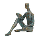 Libra Interiors Verdigris Seated Reading Man resin sculpture in antique gold and blue, cross-legged figure holding a book, shown on a plain white background.