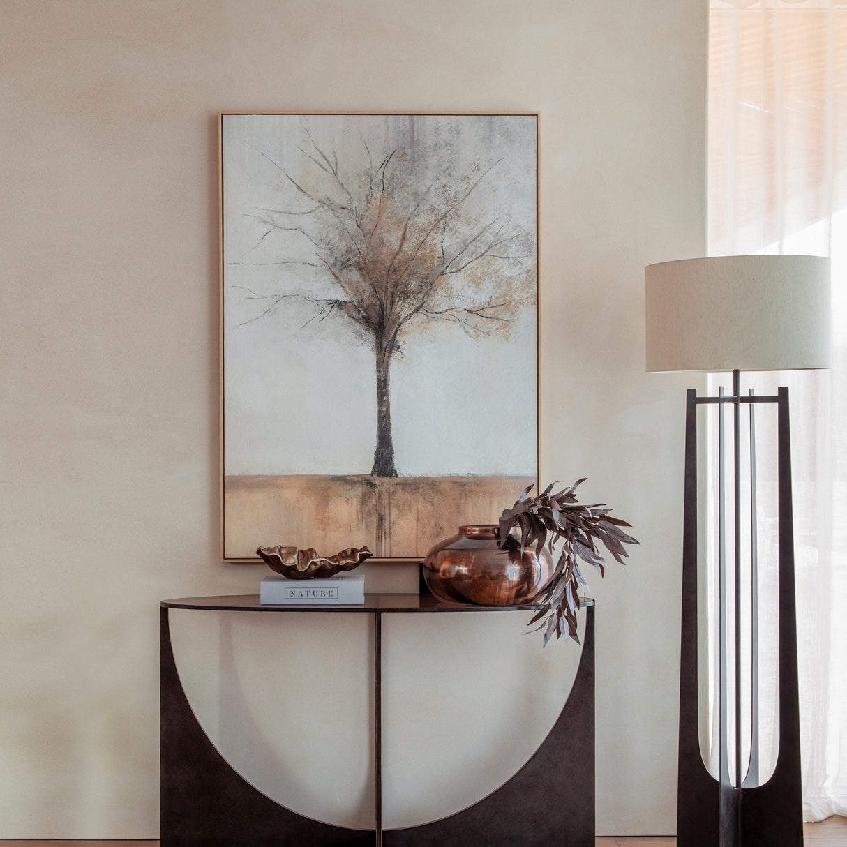 Libra Interiors Sculpted Glass & Iron Console Table in black with arched intersecting base and smoked glass top, styled with a vase and framed tree artwork.