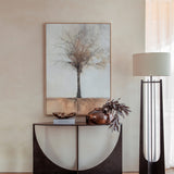 Libra Interiors Sculpted Glass & Iron Console Table in black with arched intersecting base and smoked glass top, styled with a vase and framed tree artwork.