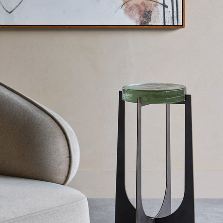 Libra Interiors Hammered Glass Arched Iron Side Table with green-tinted textured glass top and black arched base beside a light grey armchair.