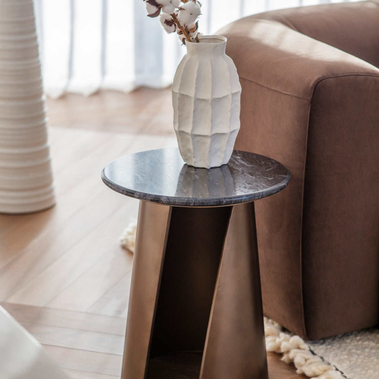 Libra Interiors Marble Top Smoked Gold Side Table with round black marble top and angular gold iron base, styled beside a brown leather sofa with a white vase.