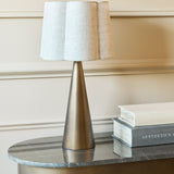 Libra Interiors Tapered Iron table lamp with smoked gold cone base and scalloped natural linen shade, styled on a marble console beside stacked books.