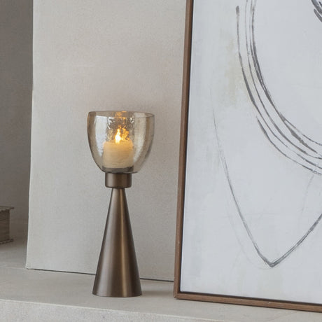 Libra Interiors Hammered Glass Tapered Hurricane Lantern in gold with a tapered iron base and copper lustre glass, styled beside abstract artwork.