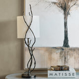 Libra Interiors Branch Iron Twig table lamp in black with hand-forged twisting stems and linen shade, styled on a side table beside a tree artwork.
