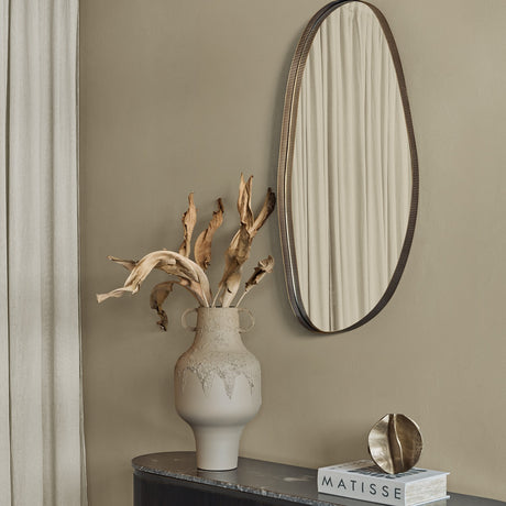 Libra Interiors Asymmetric Pebble Gilded Wall Mirror with corrugated iron frame hung portrait above a textured vase of dried leaves on a hallway console.