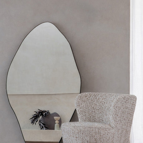 Libra Interiors Corrugated Iron Organic Wall Mirror with pebble-like silhouette and gilded oak frame, hung above a boucle armchair in a neutral living room.