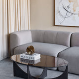 Libra Interiors Bronze Glass Sculptural Coffee Table in black with oval tinted top and curved iron base, styled with Matisse books beside a grey sofa.