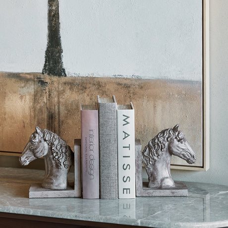 Libra Interiors Textured Resin Horse Bookends in brown bracketing design books on a marble console beneath a framed landscape artwork.