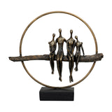 Libra Interiors Rough Cast Four Figure Circle Family Sculpture in antique gold bronze, showing four seated figures on a branch within a ring on a black base.