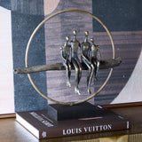 Libra Interiors Rough Cast Four Figure Circle Family Sculpture in antique gold bronze, shown on a Louis Vuitton book beside abstract wall art.