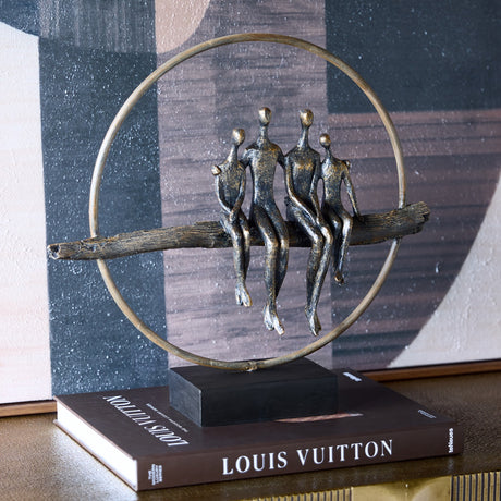 Libra Interiors Rough Cast Four Figure Circle Family Sculpture in antique gold bronze, shown on a Louis Vuitton book beside abstract wall art.