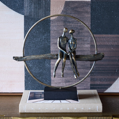 Libra Interiors Antique Gold Circle Seated Couple Sculpture on a book, showing two bronze-toned figures on a branch within a ring on a black base.