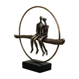 Libra Interiors Antique Gold Circle Seated Couple Sculpture in resin, two figures on a textured branch within a ring on a black base.