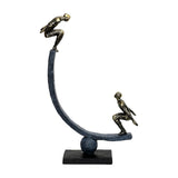 Libra Interiors Rough Cast Two Figure Balance Sculpture in bronze, with two crouched figures on a curved arc balanced over a sphere on a rectangular plinth.