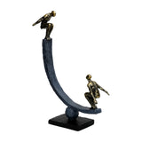 Libra Interiors Rough Cast Two Figure Balance Sculpture in bronze, with two antique gold figures crouched on a curved matt dark arc balanced on a sphere plinth.